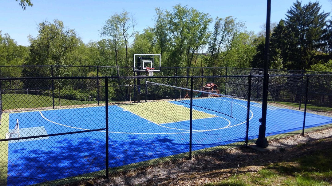 Backyard  modular basketball court with blue and green surface, featuring pickleball netting and light unit.